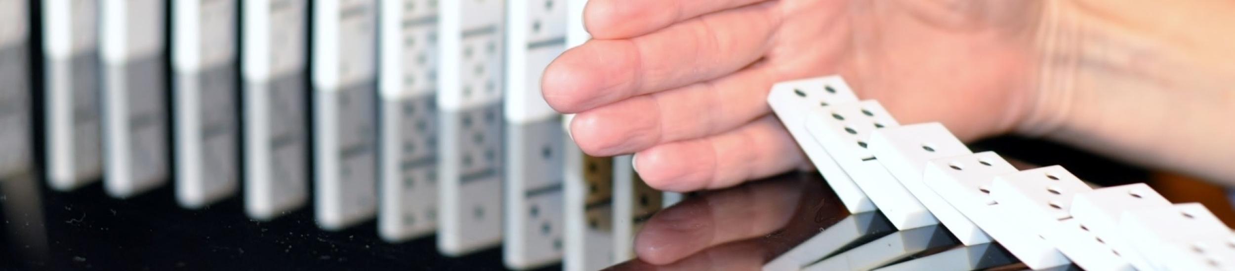 Immagine decorativa (tessere del domino che stanno cadendo in sequenza ma una mano ne blocca l'avanzamento)